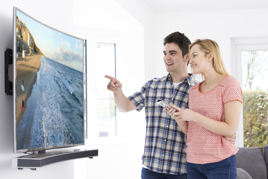 Young Couple With New Curved Screen Television At Home